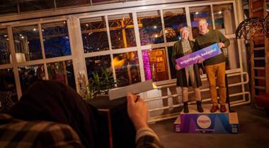 Twee personen met bord “Vrijwilligers, bedankt!” tijdens een feestelijke bijeenkomst.