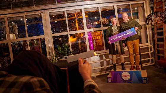 Twee personen met bord “Vrijwilligers, bedankt!” tijdens een feestelijke bijeenkomst.