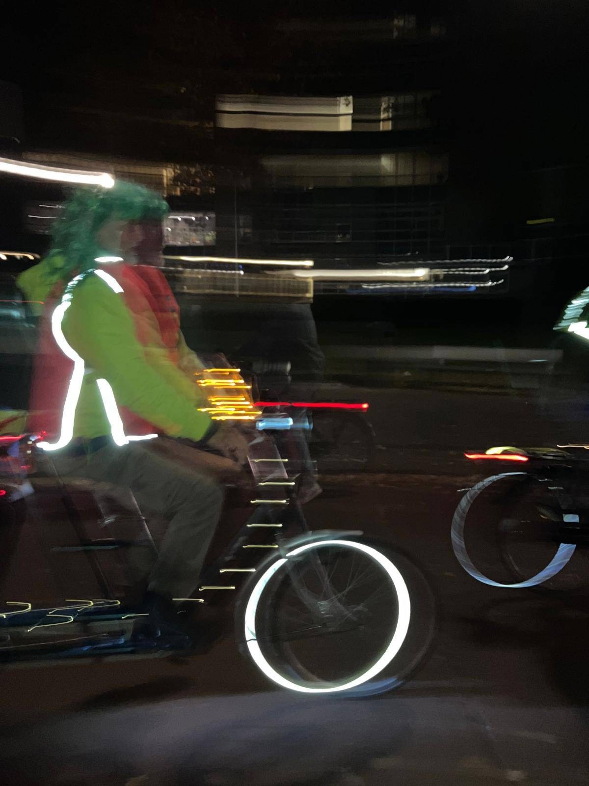 Een fietser met reflecterende kleding rijdt in het donker; de reflectie van de kleding en banden licht op.