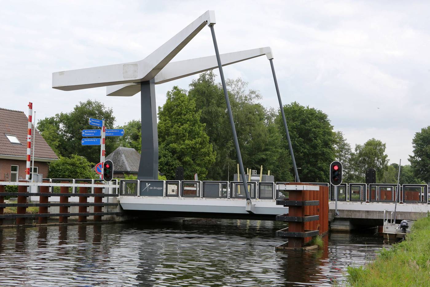 Moderne ophaalbrug over een kanaal met witte balken en verkeerslichten.