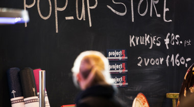 Sfeerbeeld van iemand voor krijtbord met daarop: "Pop up store en krukjes voor 85 euro en 2 voor 160 euro" 