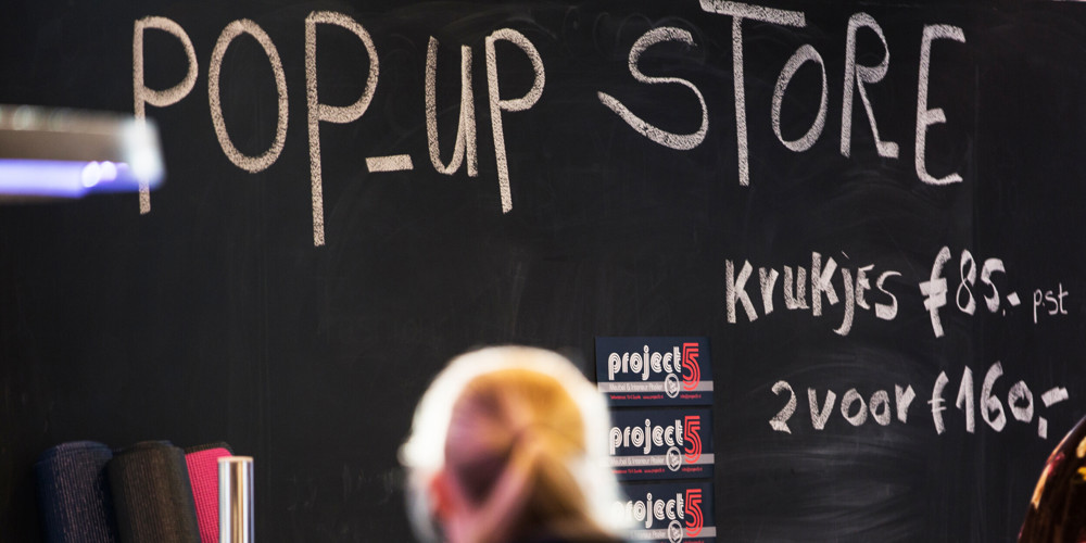 Sfeerbeeld van iemand voor krijtbord met daarop: "Pop up store en krukjes voor 85 euro en 2 voor 160 euro" 