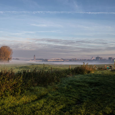 Mistig weiland met in de verte een brug