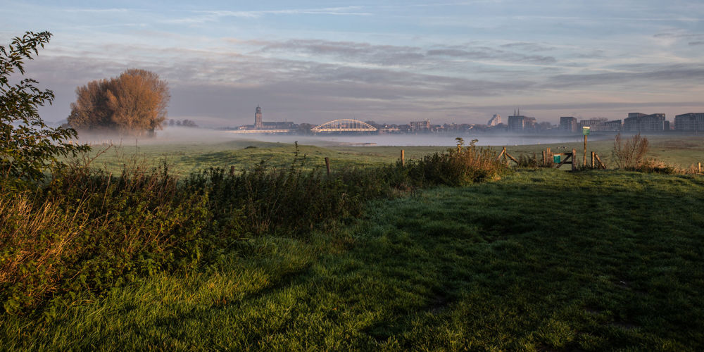 Mistig weiland met in de verte een brug