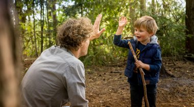 kind geeft iemand high five tussen de bomen
