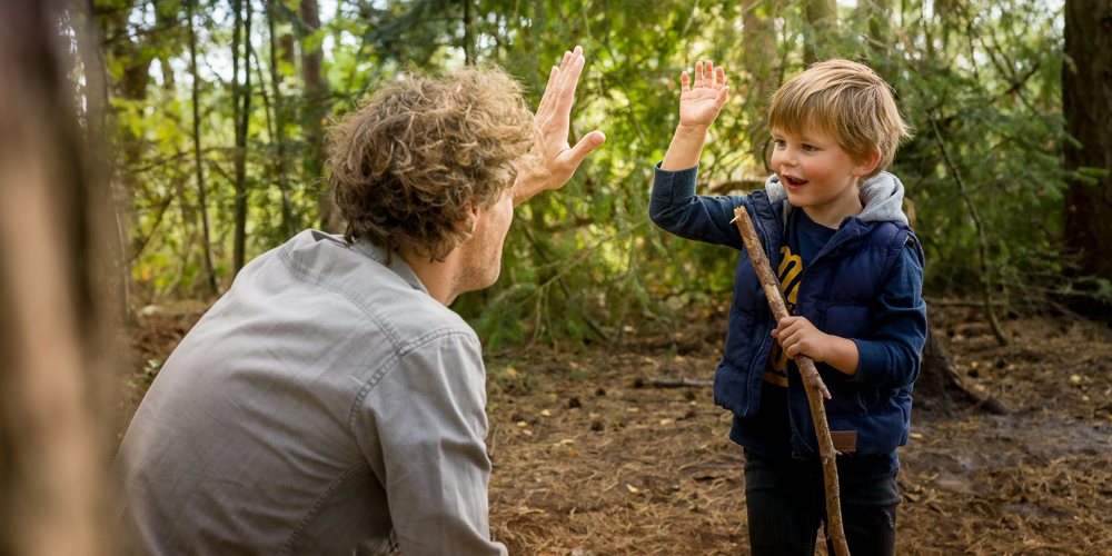 kind geeft iemand high five tussen de bomen