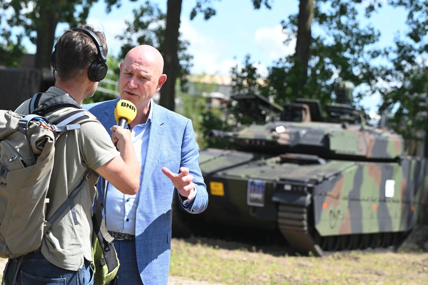 Erwin Hoogland wordt geïnterviewd door een journalist van BNR. Op de achtergrond staat een tank.