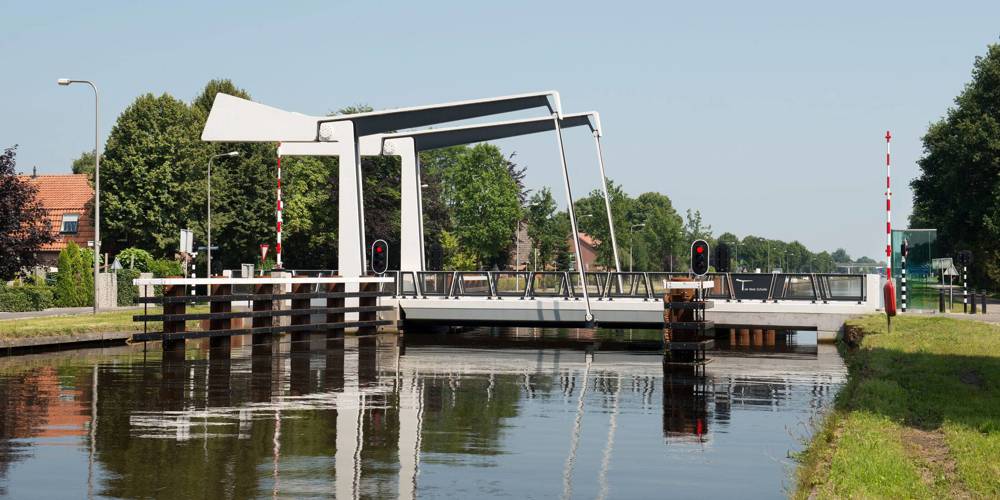 Witte ophaalbrug over een kanaal in een groene omgeving.