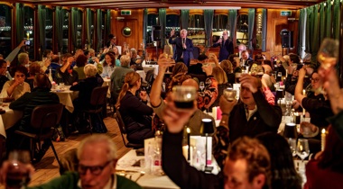 Feestzaal waarin dinertafels staan. Er is een proostmoment.