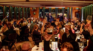 Feestzaal waarin dinertafels staan. Er is een proostmoment.