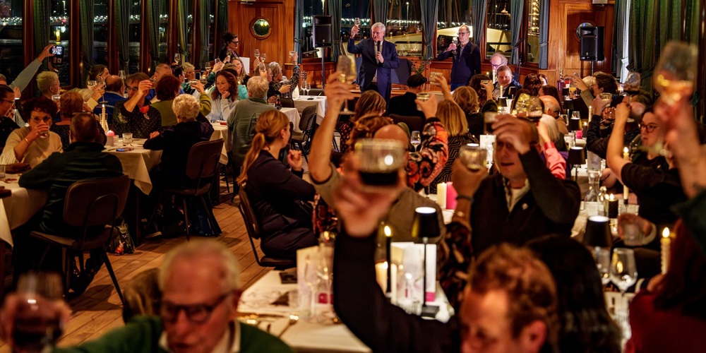 Feestzaal waarin dinertafels staan. Er is een proostmoment.