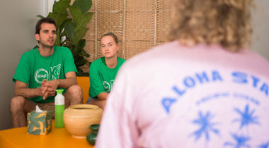 Twee vrijwilligers in een groen shirt van @ease luisteren naar iemand.