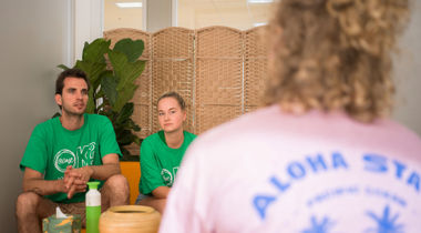 Twee vrijwilligers in een groen shirt van @ease luisteren naar iemand.