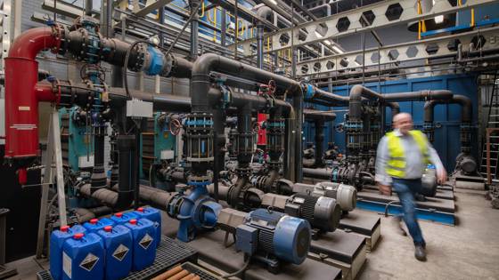 Een man in werkkleding loopt langs een installatie in een bedrijfsruimte.
