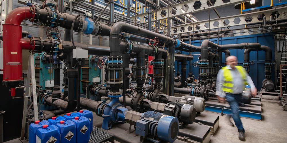 Een man in werkkleding loopt langs een installatie in een bedrijfsruimte.