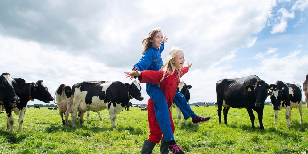 Twee kinderen in overalls in weiland tussen koeien
