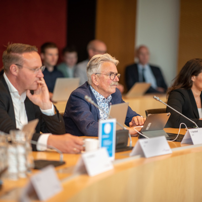 Drie mensen achter microfoons tijdens een vergadering