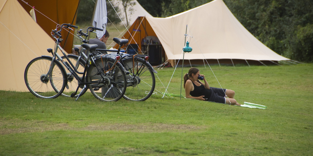 Iemand ligt naast een tent en fietsen op een groen veld