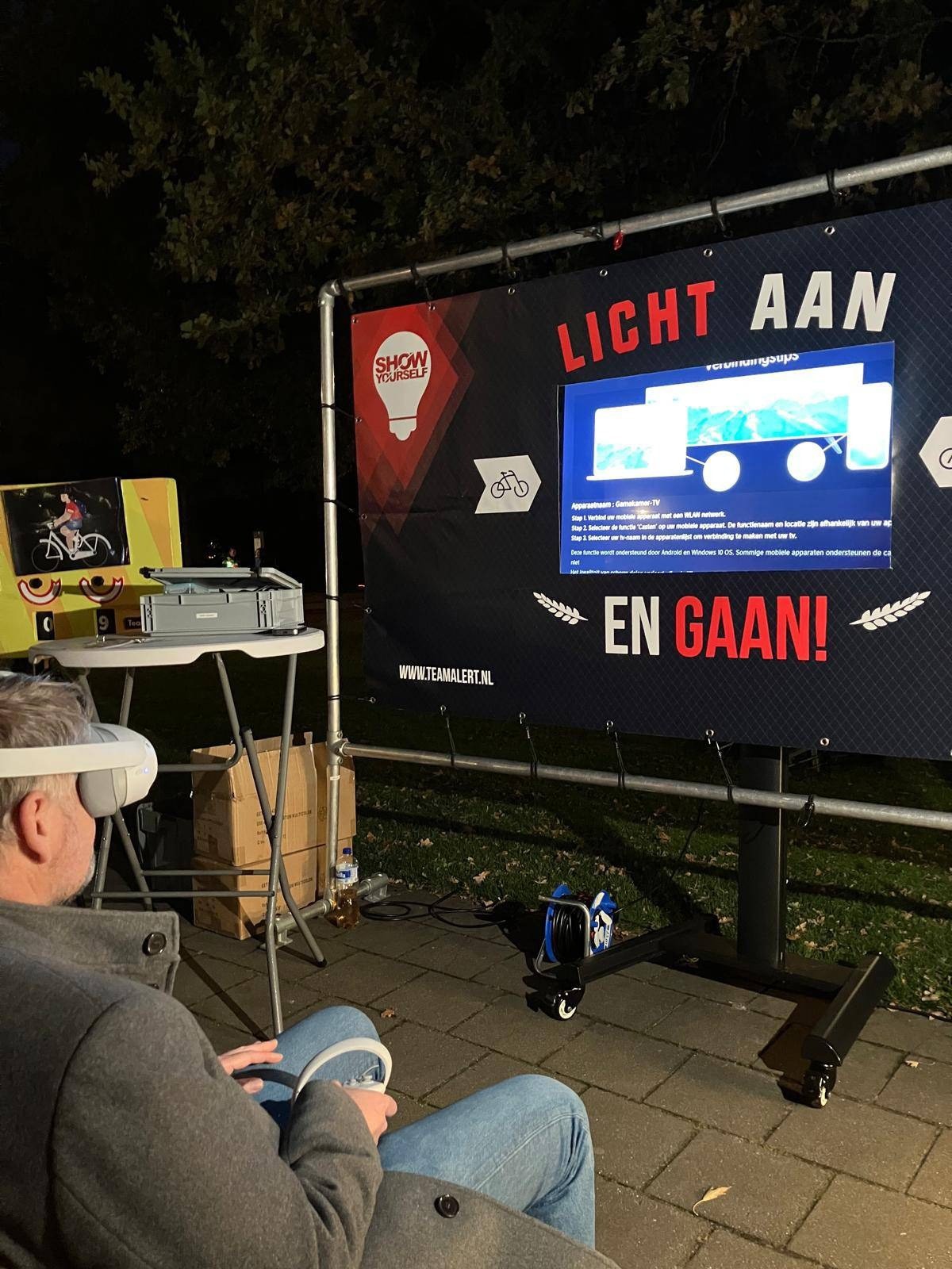Martijn Dadema met een VR-bril doet mee aan een verkeersveiligheidsactiviteit van TeamAlert met de tekst “Licht aan en gaan!” op een scherm.