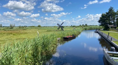 Sloot tussen landschap met kleine windmolen en aangemeerde speedbootjes naast een stijger