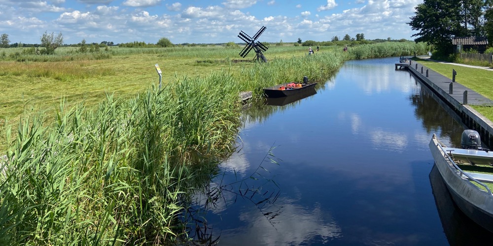 Sloot tussen landschap met kleine windmolen en aangemeerde speedbootjes naast een stijger
