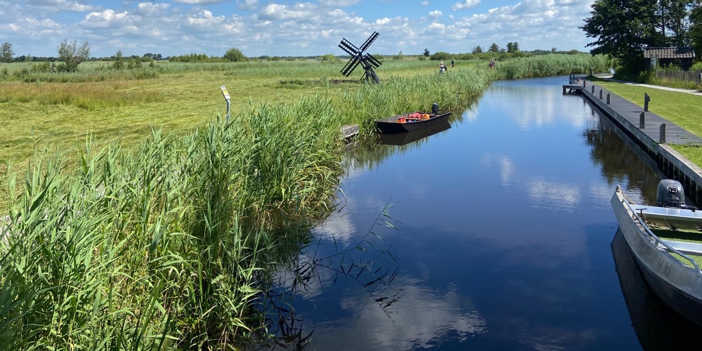 Sloot tussen landschap met kleine windmolen en aangemeerde speedbootjes naast een stijger
