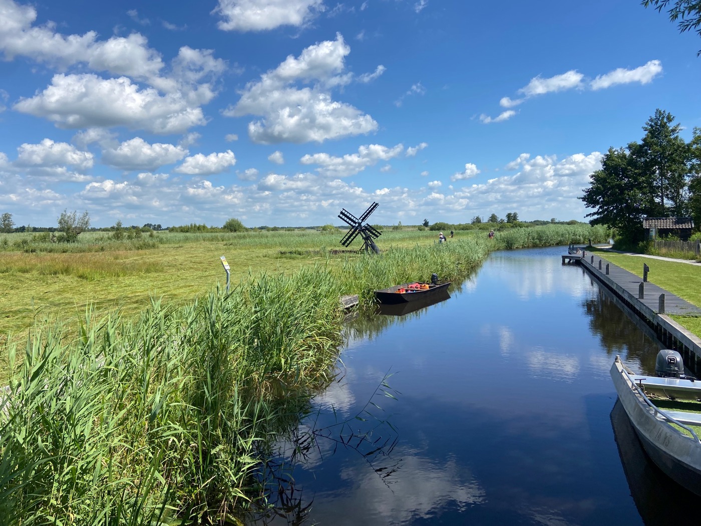 Sloot tussen landschap met kleine windmolen en aangemeerde speedbootjes naast een stijger