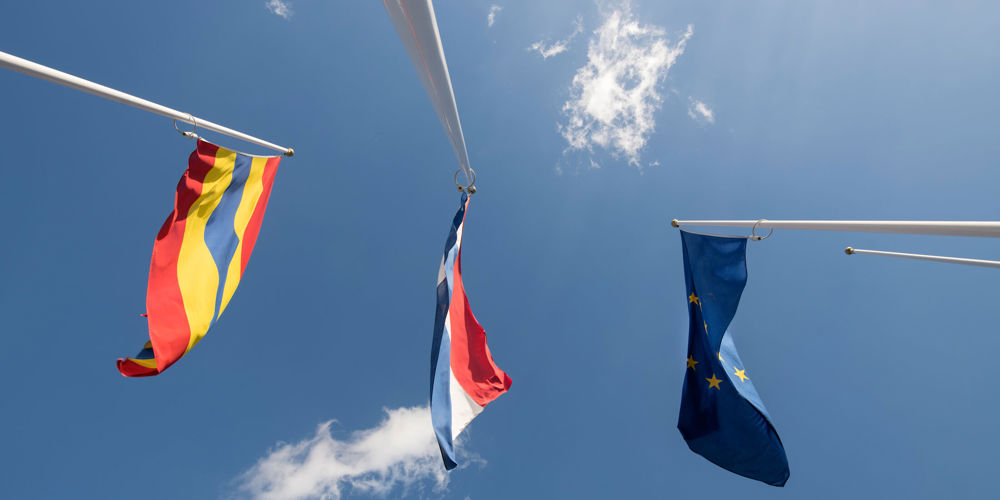 foto van onder naar boven van drie vlaggen: de Overijsselse, Nederlandse en Europese