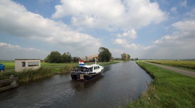 Foto van boot die vaart op sloot tussen landschap en weg