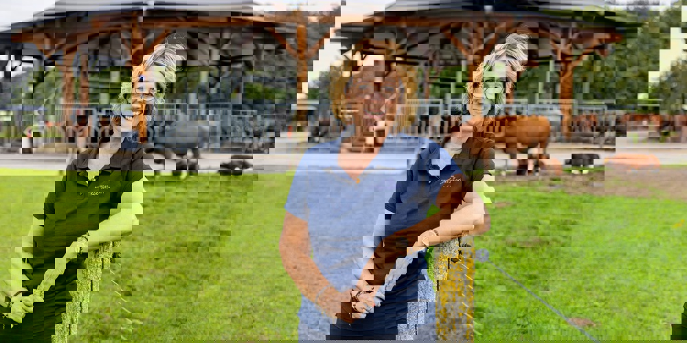 Simone Koggel bij een paaltje met daarachter koeien bij een 'stal'