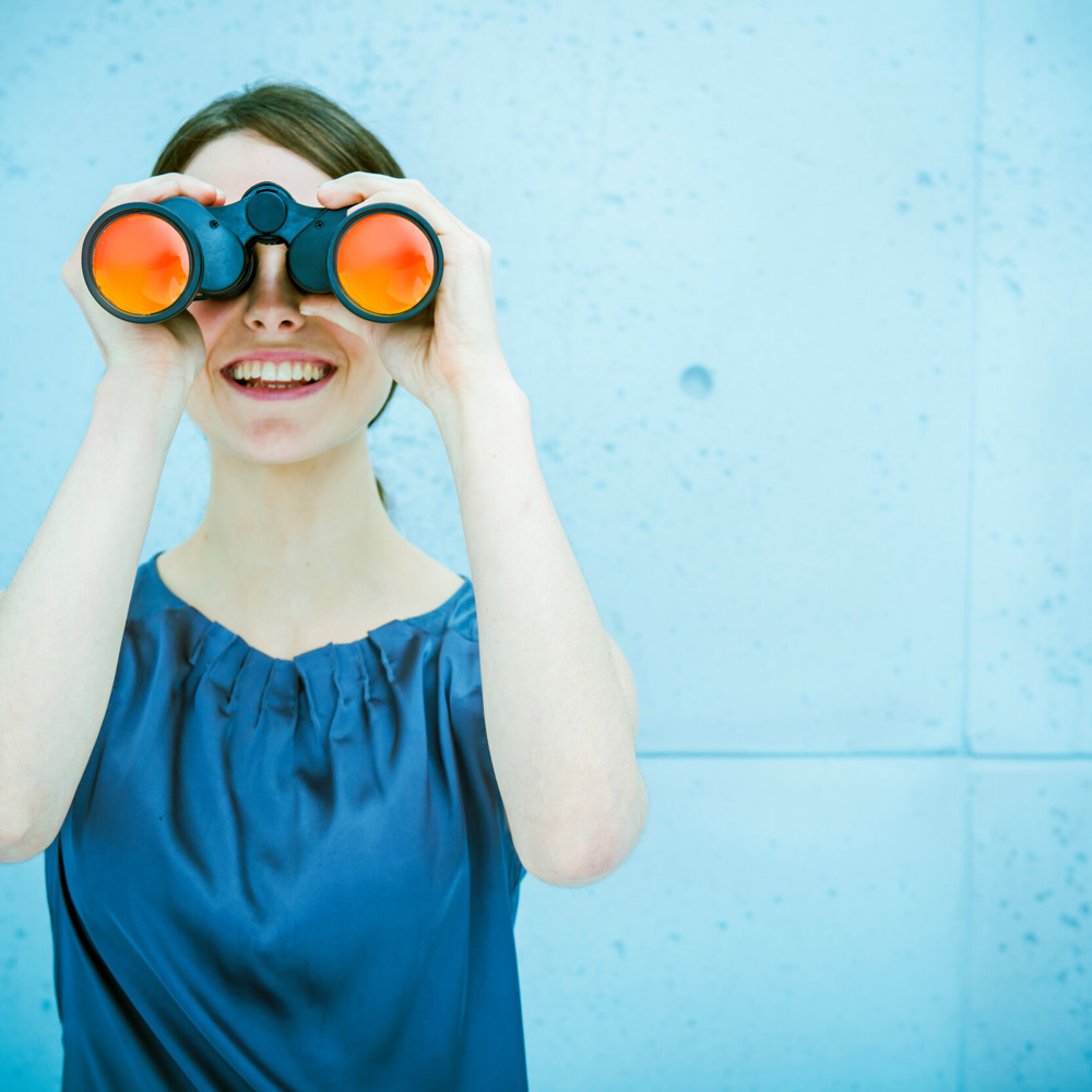 Vrouw in blauw met verrekijker en blauwe achtergrond