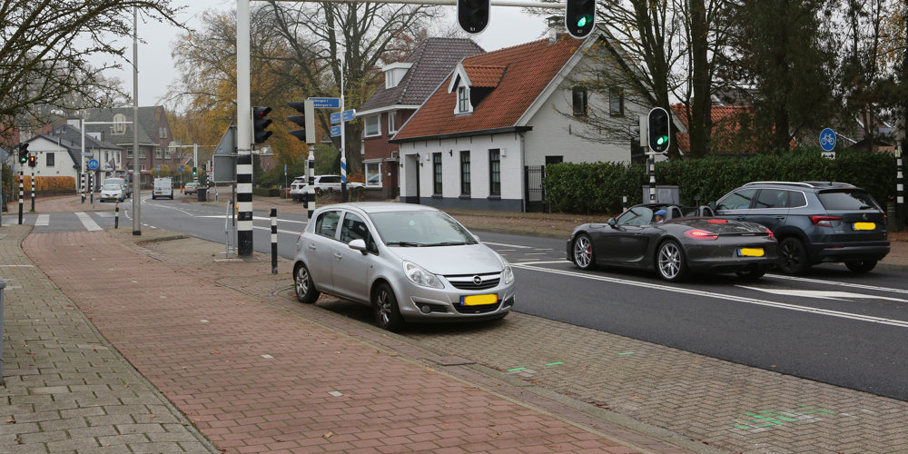 Vloedbelt 26 geparkeerde auto en verschillende auto's staan voor de stoplichten. Aan de kant staan huizen.