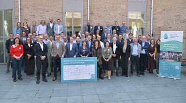 Vertegenwoordigers van de organisaties die het manifest hebben ondertekend op een groepsfoto voor een muur van een gebouw. Voor hen staat een bord met de tekst "Samen bouwen wij aan waterzuinige wijken van de toekomst." En daaronder de namen van de ondertekenaars (niet goed leesbaar op de foto). Rechts naast hen staat een bord van de Bouwtafel waterzuinige wijken met de tekst "Samen voor waterzuinige wijken."