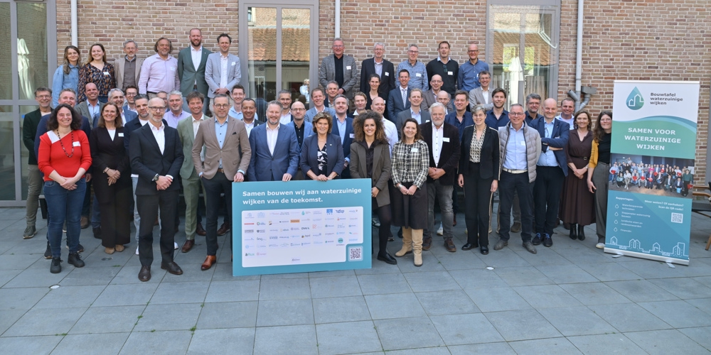 Vertegenwoordigers van de organisaties die het manifest hebben ondertekend op een groepsfoto voor een muur van een gebouw. Voor hen staat een bord met de tekst "Samen bouwen wij aan waterzuinige wijken van de toekomst." En daaronder de namen van de ondertekenaars (niet goed leesbaar op de foto). Rechts naast hen staat een bord van de Bouwtafel waterzuinige wijken met de tekst "Samen voor waterzuinige wijken."