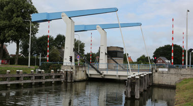 Brug Vriezenveen over water. Oevers aan beide kanten. 4 rood-witte slagbomen, 2 aan beide kanten van de brug