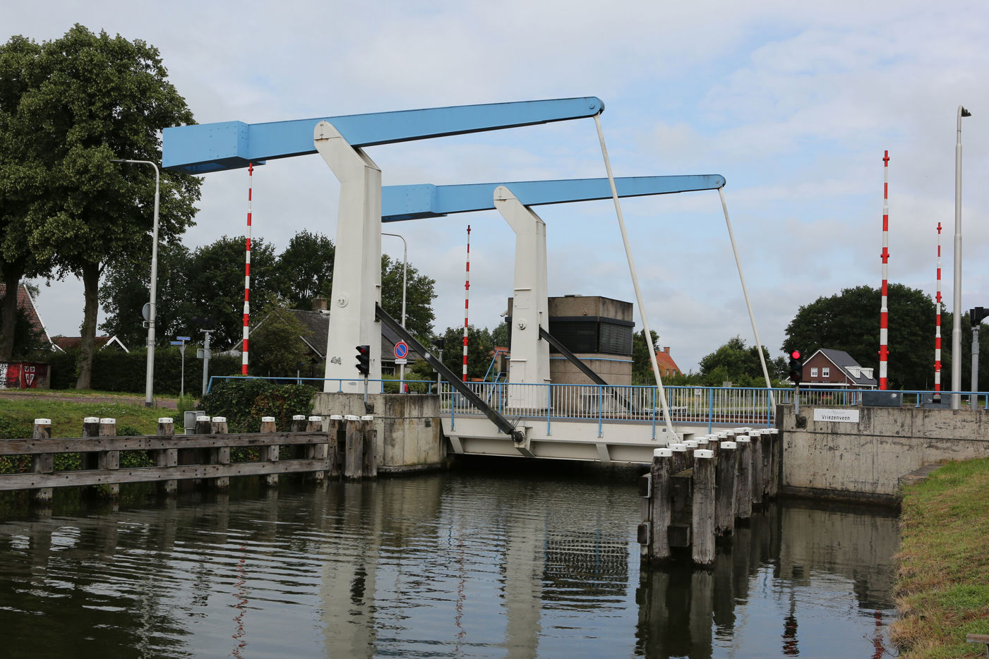 Brug Vriezenveen over water. Oevers aan beide kanten. 4 rood-witte slagbomen, 2 aan beide kanten van de brug