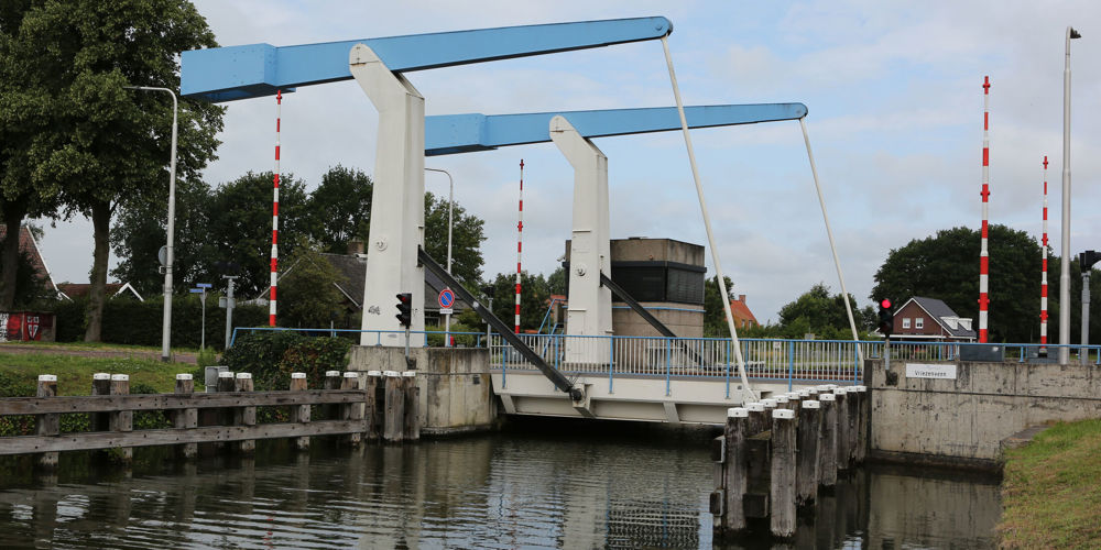 Brug Vriezenveen over water. Oevers aan beide kanten. 4 rood-witte slagbomen, 2 aan beide kanten van de brug