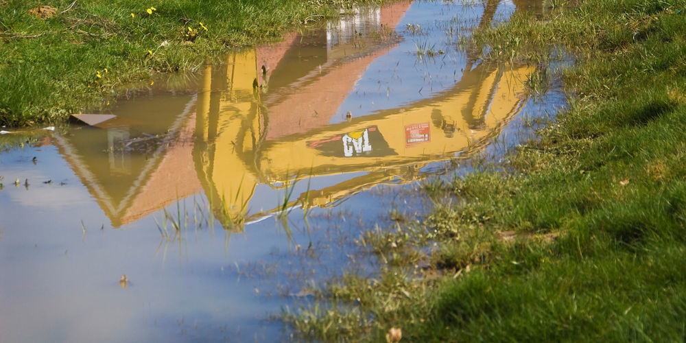 Plas in het gras met weerspiegeling van graafmachine en woning in plas