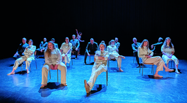 Groep mensen in witte kleren geposeerd op stoel op podium