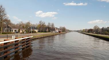 Kanaal met huizen, bomen en een ruiter op een zonnige dag.