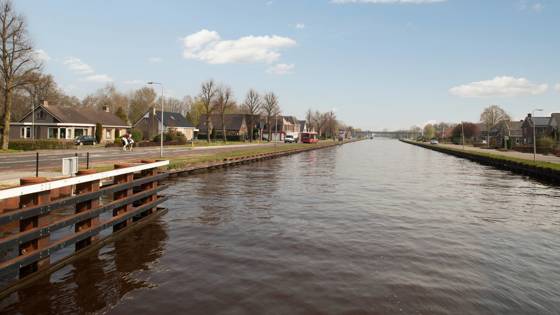 Kanaal met huizen, bomen en een ruiter op een zonnige dag.