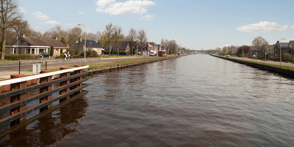 Kanaal met huizen, bomen en een ruiter op een zonnige dag.