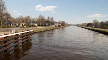 Kanaal met huizen, bomen en een ruiter op een zonnige dag.