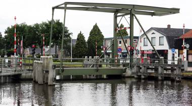 Groene ophaalbrug over een kanaal in een dorpsomgeving.