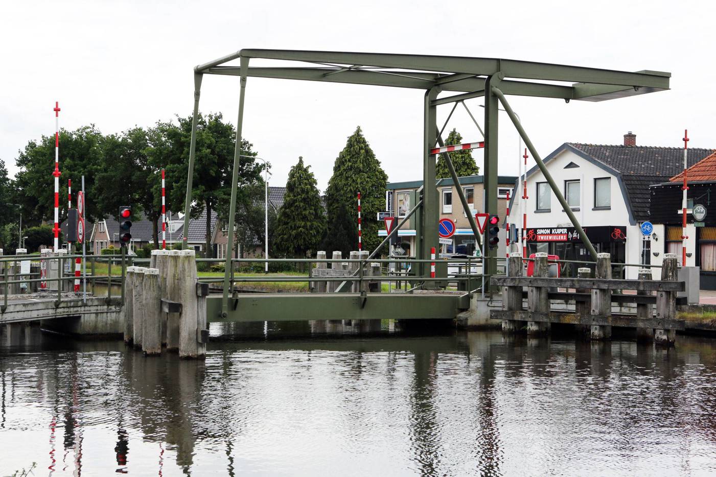 Groene ophaalbrug over een kanaal in een dorpsomgeving.