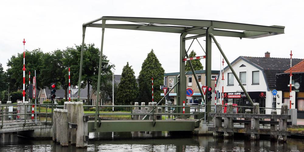 Groene ophaalbrug over een kanaal in een dorpsomgeving.