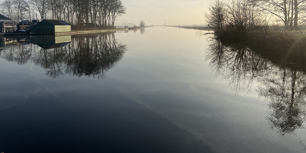 Kanaal bij het ochtendlicht met reflecterende bomen langs de rand in de winter