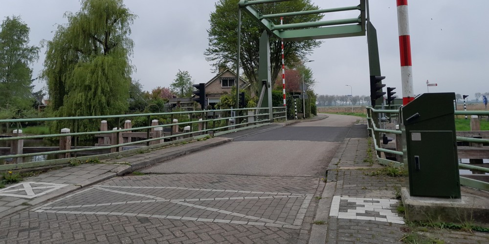 Hoogwegbrug Ossenzijl: ophaalbrug over een kanaal met bomen en een huis op de achtergrond.