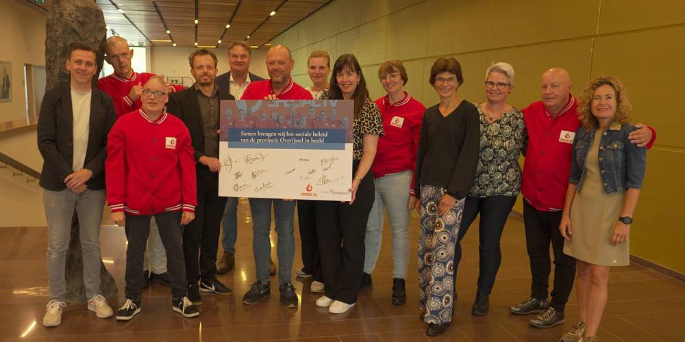 Een groep mensen, deels gekleed in rode jassen van Special TV, poseert met een groot, ondertekend bord van SpecialTV in het provinciehuis van provincie Overijssel.