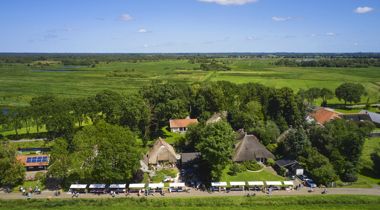 vogel perspectief foto van landschap met bomen en op voorgrond witte kraampjes met mensen op een lange strook weg